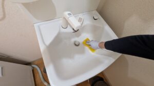 広島市内で洗面所の掃除を行う便利屋万のスタッフ。スポンジを使い、洗面ボウルの水垢や汚れを丁寧に手洗いしています。家事代行・ハウスクリーニングの実績。