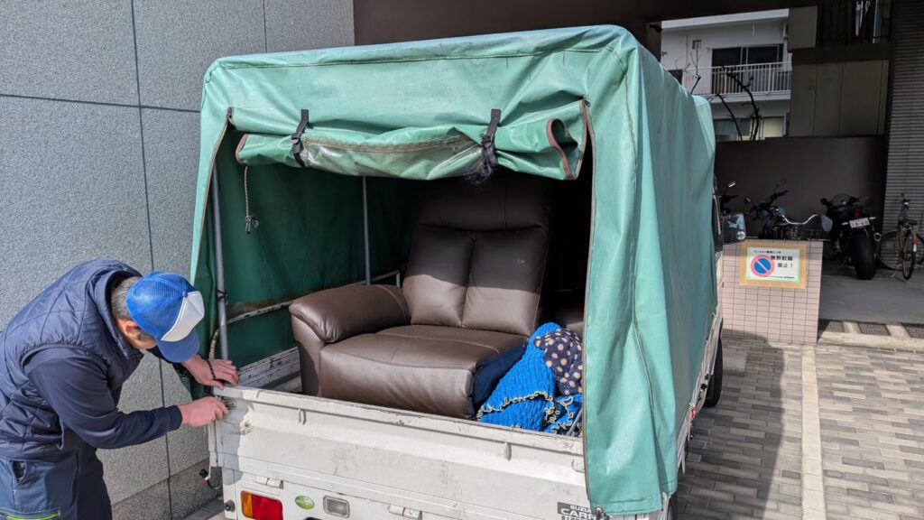 広島市中区舟入にて、自宅から介護施設へソファを運搬する様子。便利屋万のスタッフ2名で、軽トラックに積み込み固定している作業風景。